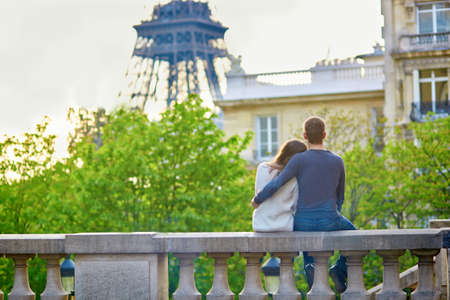 Beautiful romantic couple in Paris sitting outdoors, hugging and looking at the Eiffel towerの写真素材
