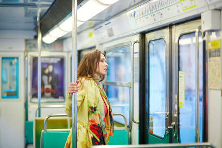 Young beautiful Parisian woman travelling in a subway train, standing near the windowの写真素材