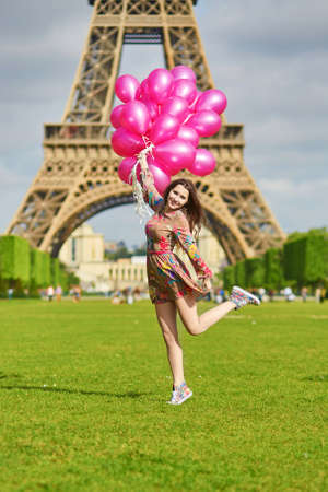 Beautiful young woman in Paris, near the Eiffel tower jumping happily with huge bunch of pink...