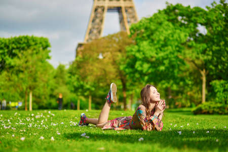 Happy young girl in colorful dress lying on the grass near the Eiffel tower in Paris