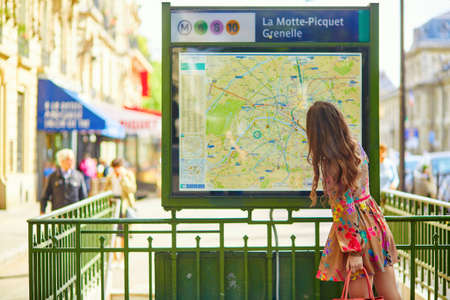 Young beautiful Parisian woman near the subway plan, looking for the directionのeditorial素材