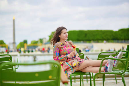 Young Parisian woman in the Tuileries garden, sitting on a chair and eating ice creamの写真素材