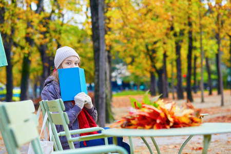 Girl reading a book in an outdoor cafe on a bright fall day in Paris