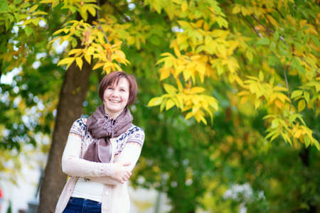 Beautiful middle aged woman outdoors on a bright fall day, yellow autumn leaves in the backgroundの写真素材