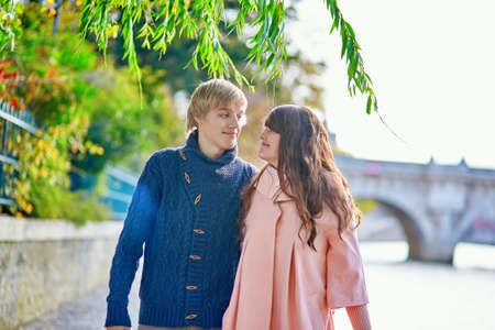 Young dating couple in Paris on a bright fall day, walking together by the Seine, colorful autumn leaves in the backgroundの写真素材