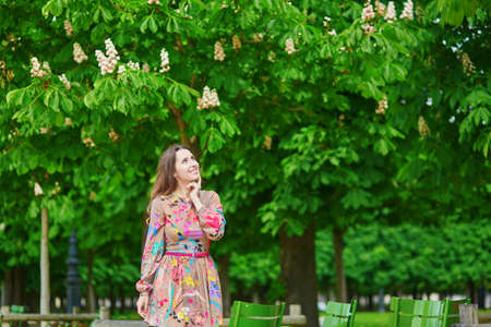 Beautiful young woman in the Tuileries garden, walking under chestnut trees in full bloomの写真素材