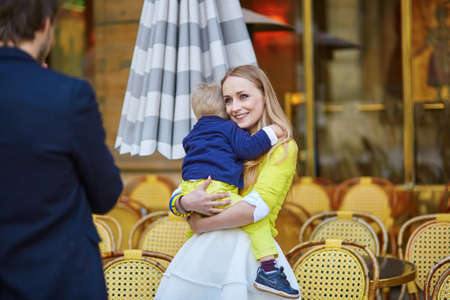Happy family spending fun together in an outdoor Parisian cafe, mother is hugging her little sonの写真素材