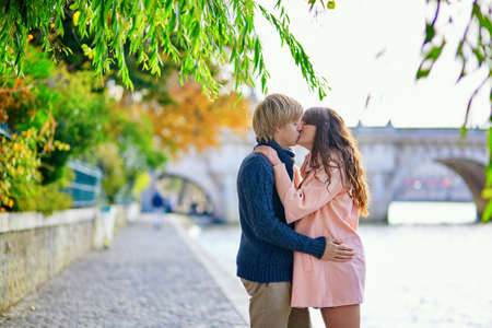 Young dating couple in Paris on a bright fall day, walking together by the Seine, colorful autumn leaves in the backgroundの写真素材