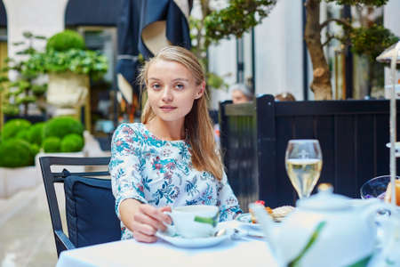 Beautiful young woman enjoying afternoon tea with selection of fancy cakes and sandwiches in a luxury Parisian restaurantの写真素材
