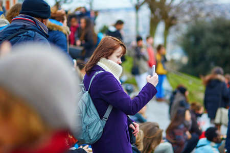 Beautiful young girl walking in Paris and taking pictures with her mobile phoneの写真素材