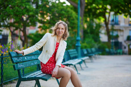 Beautiful young woman in red polka dot dress sitting on bench in Marais, Paris, Franceの写真素材