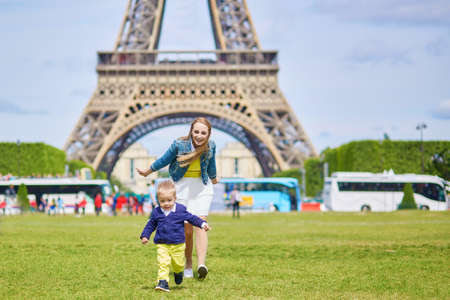Beautiful young mother and her adorable toddler son having fun together near the Eiffel tower in Paris, boy is running from his mommyの写真素材