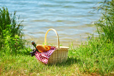 Picnic basket with food and cider bottle near the waterの写真素材