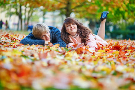 Young dating couple in Paris on a bright fall day sitting on the ground in autumn leaves