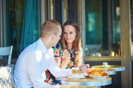 Young romantic couple drinking coffee and eating traditional French croissants in a cozy outdoor cafe in Paris, Franceの写真素材