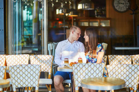 Young romantic couple drinking coffee and eating traditional French croissants in a cozy outdoor cafe in Paris, Franceの写真素材