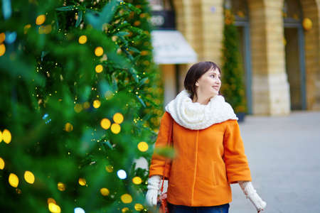 Cheerful young woman in Paris on a winter day, walking in the street decorated for holidays and enjoying Christmas seasonの写真素材