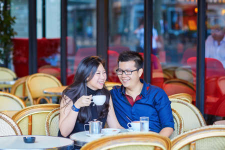 Young romantic Asian couple drinking coffee in a cozy outdoor cafe in Paris, Franceの写真素材