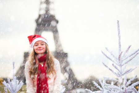 Girl in Santa hat near the Eiffel tower in Paris during Christmas time during snowfallの写真素材
