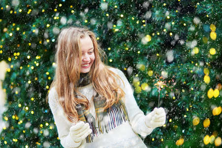 Cheerful girl on a Parisian street decorated for Christmas during snowfallの写真素材