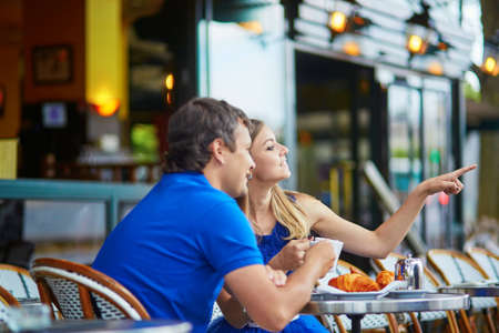 Beautiful young couple of tourists drinking coffee and eating traditional French croissants in Parisian street cafeの写真素材