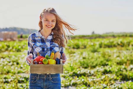 Happy young woman holding wooden crate with fresh organic vegetables from farmの写真素材