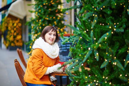 Beautiful young girl in an outdoor Parisian cafe on a winter day, drinking hot beverageの写真素材