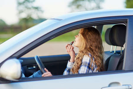 Beautiful blond woman applying lipstick in a car while drivingの写真素材