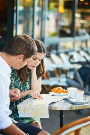 Young romantic couple drinking coffee, eating traditional French croissants and planning their itinerary using map in a cozy outdoor cafe in Paris, Franceの写真素材