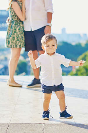 Happy little bay making his first steps, parents are hugging in the backgroundの写真素材