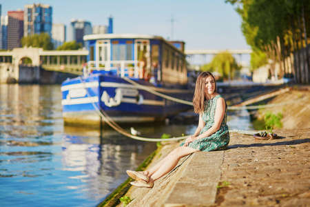 Happy young girl sitting on the bank of the Seine and enjoying her trip to Paris, Franceの写真素材