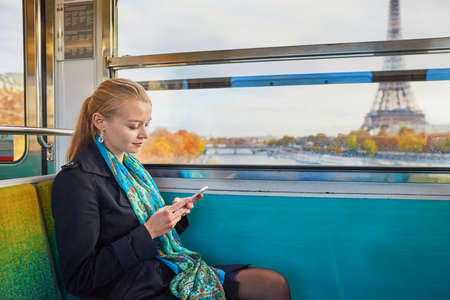 Beautiful young woman travelling in a train of Parisian underground and using her mobile phone. Eiffel tower is behind the windowの写真素材