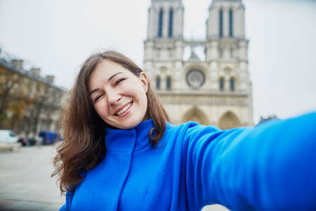 Beautiful young tourist in Paris on a fall day, making funny selfie with Notre-Dame cathedralの写真素材
