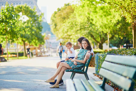 Happy family of three sitting on the bench in park near the Eiffel tower and enjoying their vacation in Paris, Franceの写真素材
