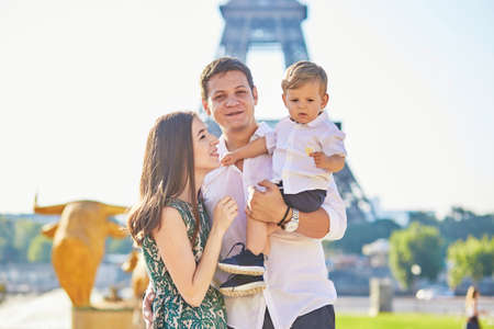 Happy family of three standing in front of the Eiffel tower and enjoying their vacation in Paris, Franceの写真素材
