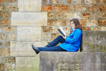 Beautiful young girl reading a book on the Seine embankment in Parisの写真素材