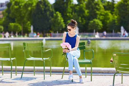 Beautiful young Parisian woman in blue blouse with bunch of pink peonies in the Tuileries garden of Parisの写真素材