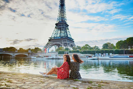 Beautiful twin sisters in red and black polka dot dresses in front of the Eiffel tower near the river Seine in Paris, Franceの写真素材