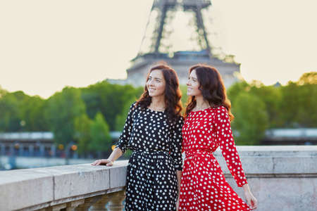 Beautiful twin sisters in red and black polka dot dresses in front of the Eiffel tower in Paris, Franceの写真素材