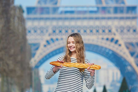 Beautiful young girl with fresh tasty traditional French bread (baguette) near the Eiffel tower
