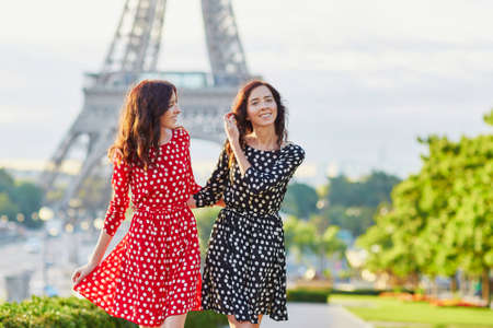 Beautiful twin sisters in red and black polka dot dresses in front of the Eiffel tower in Paris, Franceの写真素材
