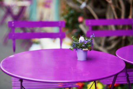 Purple table of Parisian outdoor cafe decorated with little bucket, flowers and Easter egg