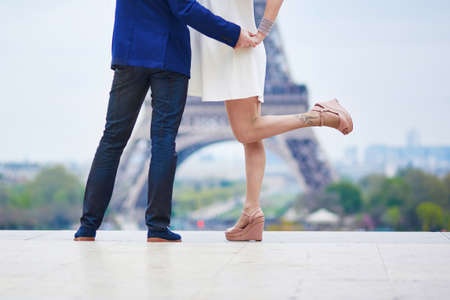Closeup of man's and woman's legs during a kiss on a date, Eiffel tower in the background.