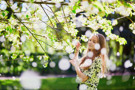 Beautiful girl in cherry blossom garden on a spring day, flower petals falling from the tree