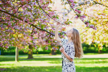 Beautiful young woman enjoying sunny day in park during cherry blossom season on a nice spring dayの写真素材