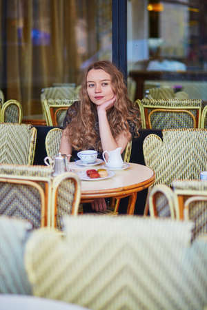 Beautiful Parisian woman in cafe, drinking coffee and eating macaroons, traditional French dessertの写真素材