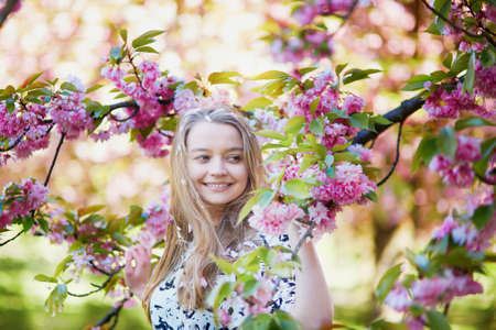 Beautiful young woman enjoying sunny day in park during cherry blossom season on a nice spring day