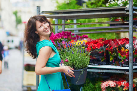Cheerful happy young French woman selecting flowers on market, holding a flower pot with lavender. Paris, Franceの写真素材