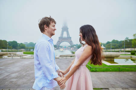 Beautiful romantic couple in love near the Eiffel tower in Paris on a cloudy and foggy rainy dayの写真素材
