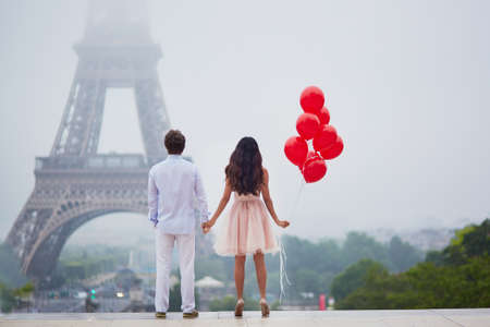 Beautiful romantic couple in love with bunch of red balloons together near the Eiffel tower in Paris on a cloudy and foggy rainy dayの写真素材